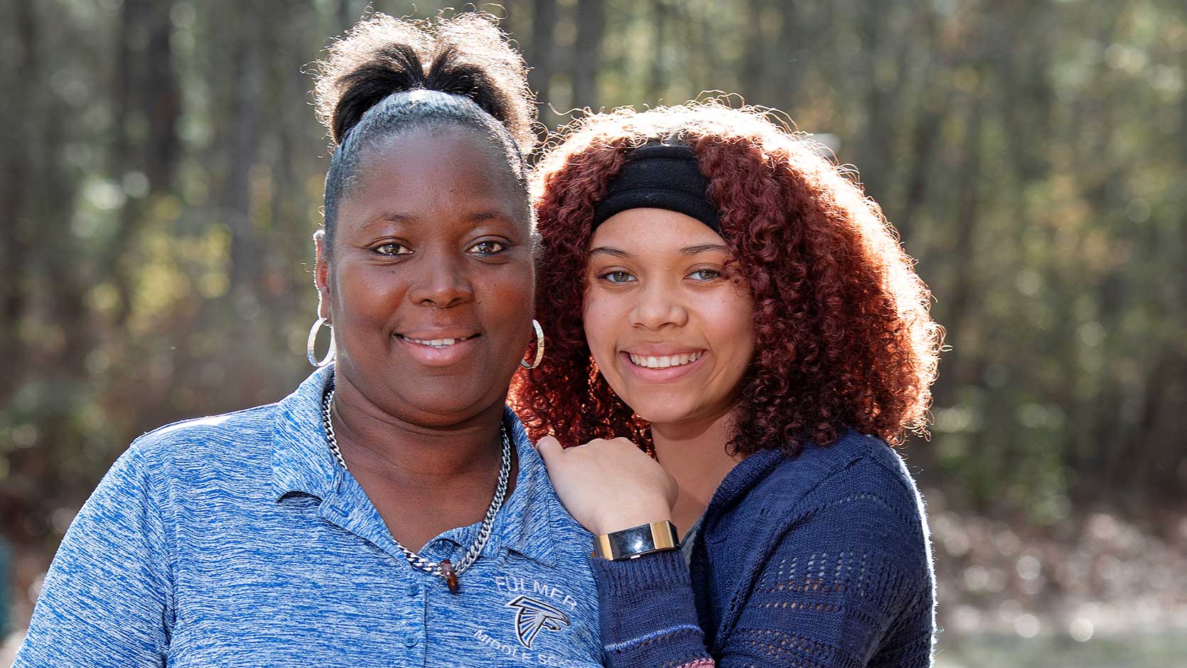 Two women smiling in front of a forested backdrop.
