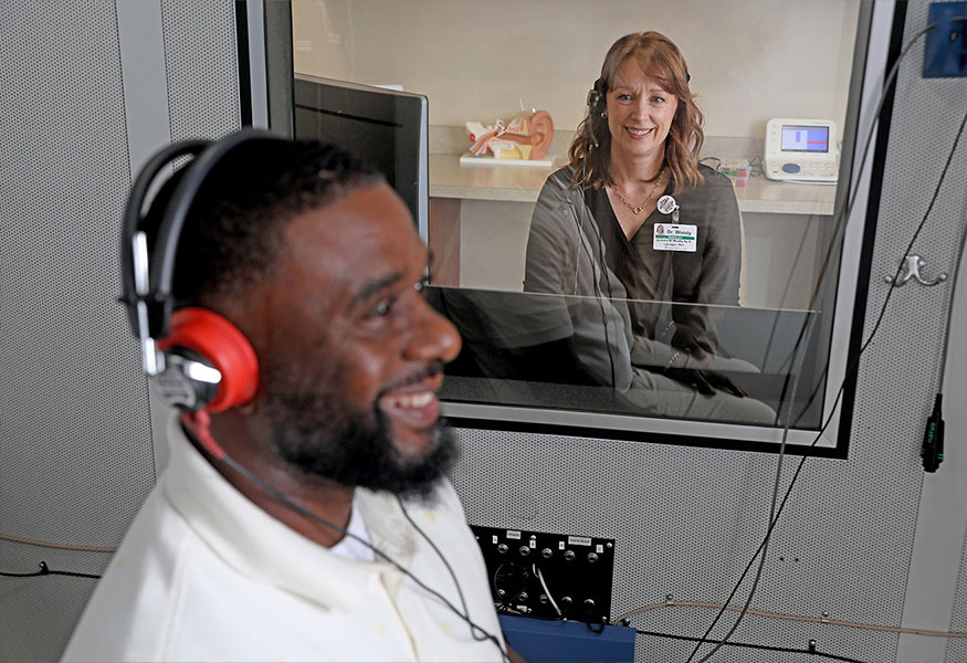 A patient wearing headphones while an audiologist performs a hearing test.