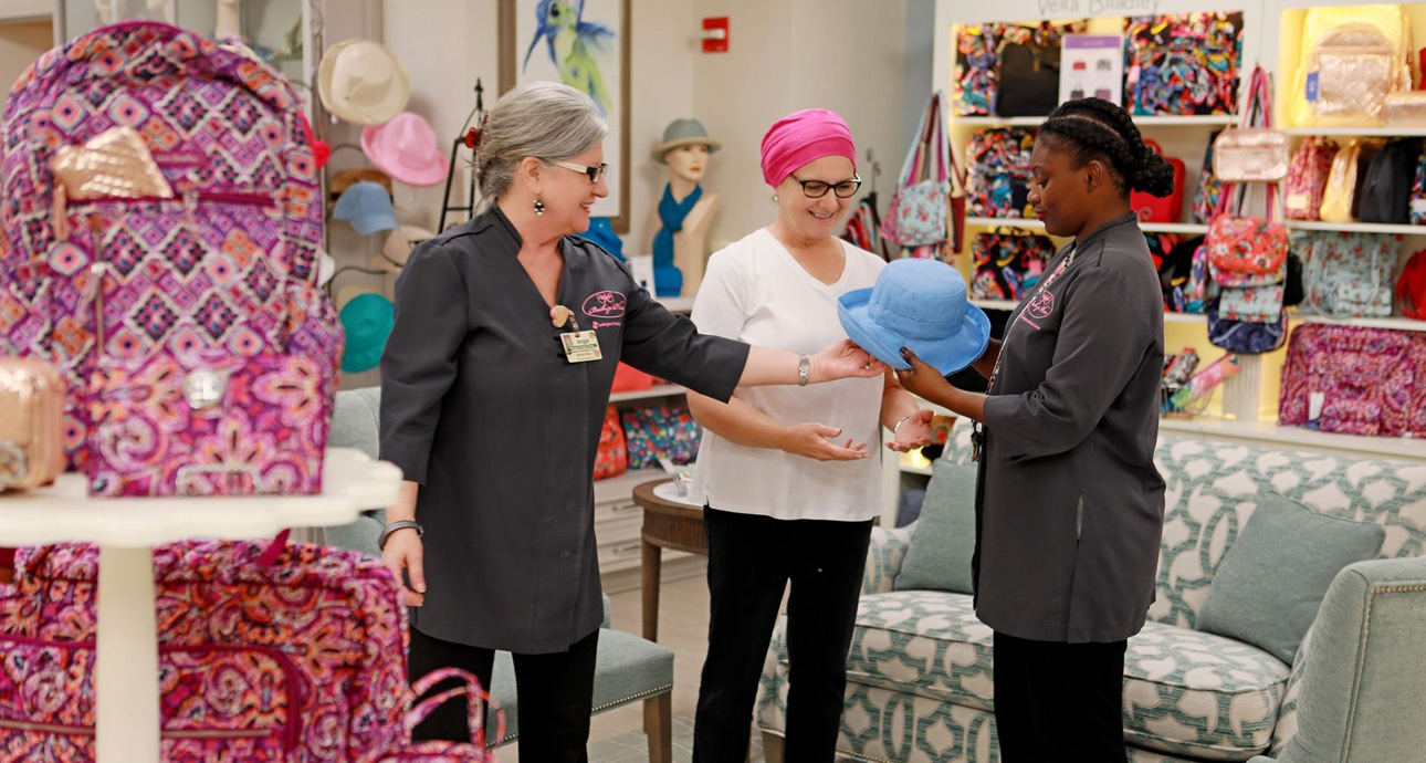 Smiling employees and a cancer patient looking at hats in a boutique selling colorful bags, hats and accessories.