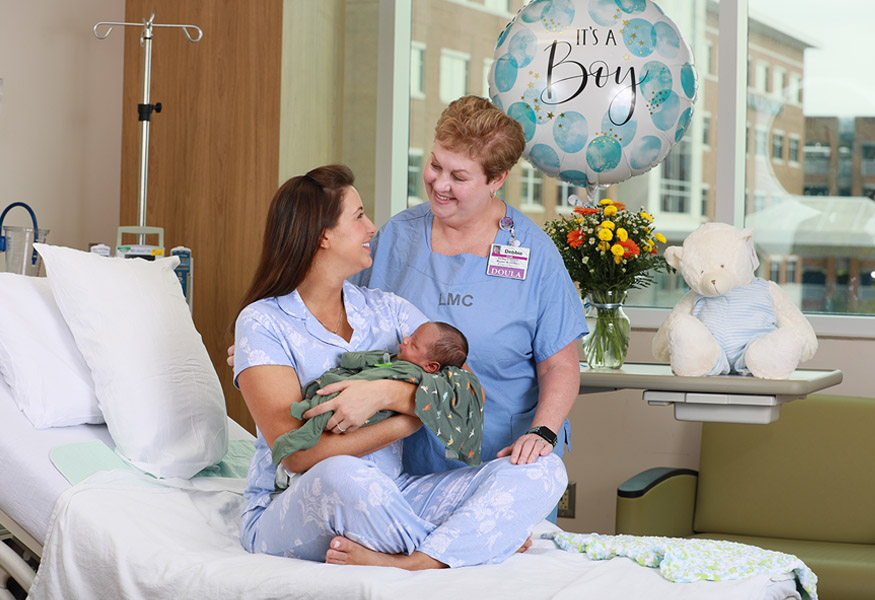 A doula smiles at a mother who is holding her newborn baby. 