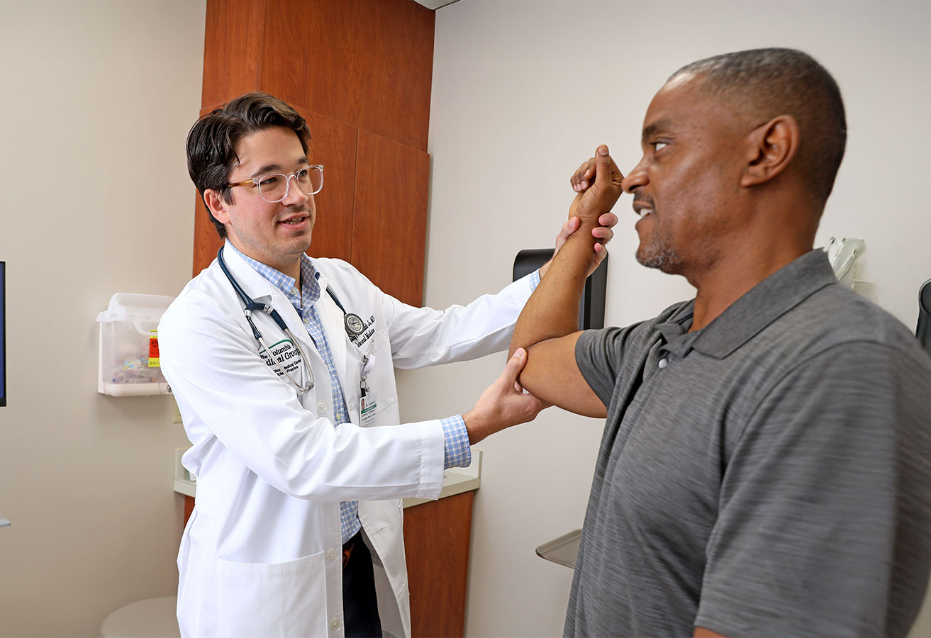 An adult primary care doctor looking at a patient's elbow.