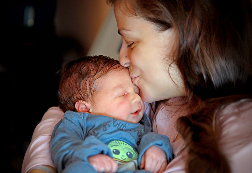 A smiling mother kissing the top of her newborn's head. 